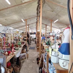 Overzicht van inboedelhal met houten stellingen, huishoudelijke artikelen en meubilair verspreid over de vloer