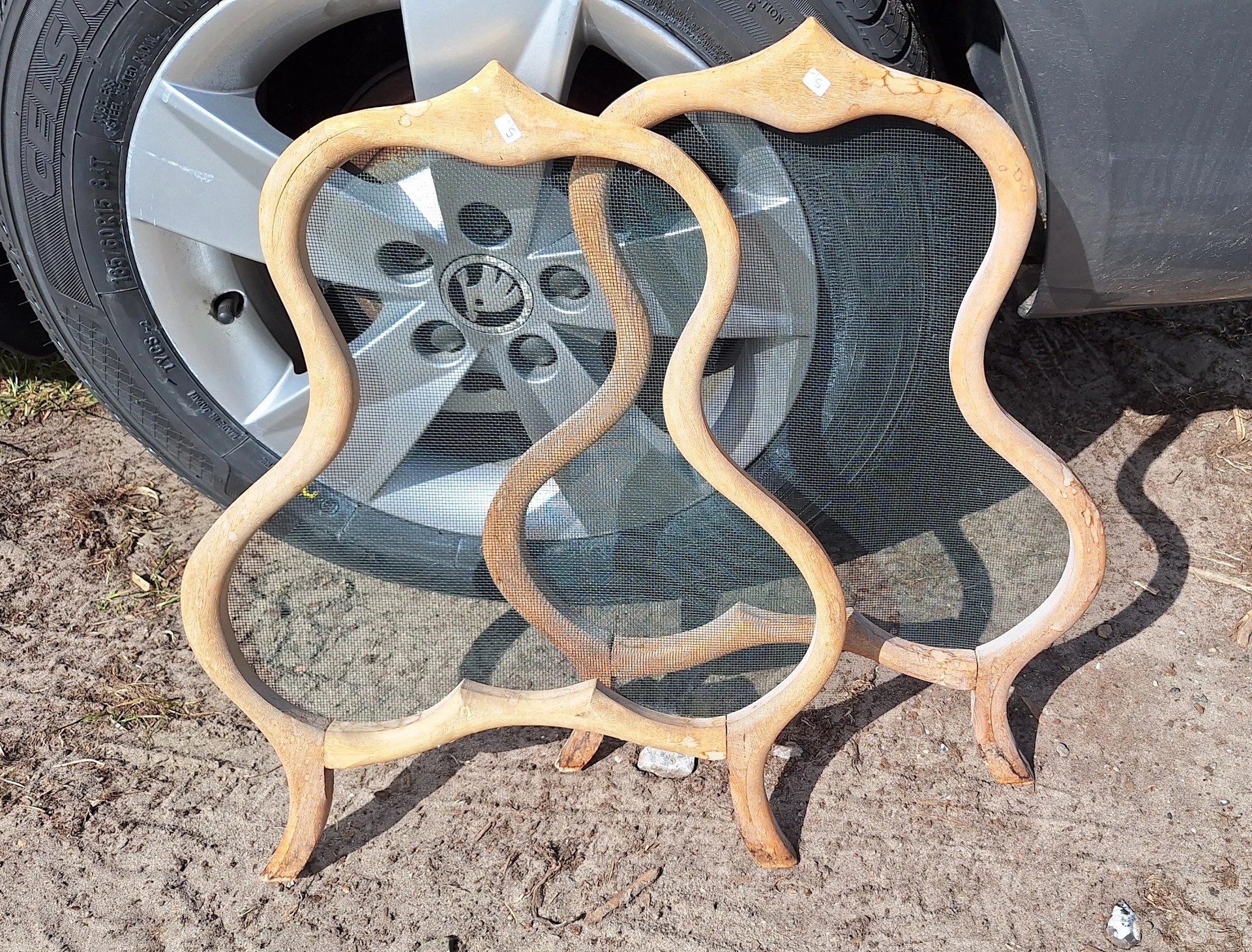 Houten sidetable of krukje met golvende randen tegen autowiel op parkeerplaats