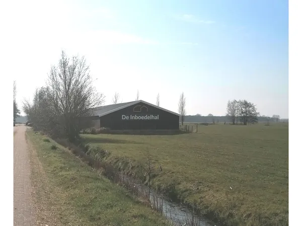 Zwart bedrijfsgebouw 'De Inboedelhal' aan landweg met weiland ernaast