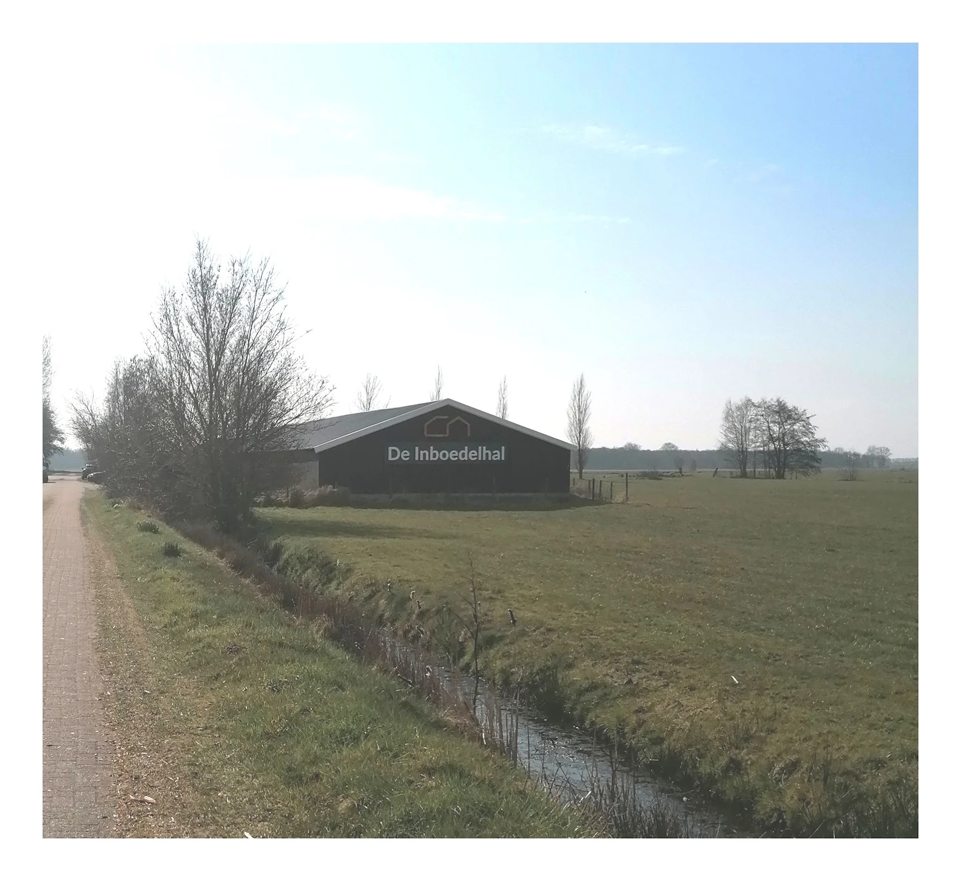 Zwart bedrijfsgebouw 'De Inboedelhal' aan landweg met weiland ernaast