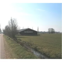 Zwart bedrijfsgebouw 'De Inboedelhal' aan landweg met weiland ernaast