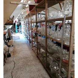 Gangpad in kringloopwinkel met glazen vitrinekasten vol glaswerk en ander inboedelgoed