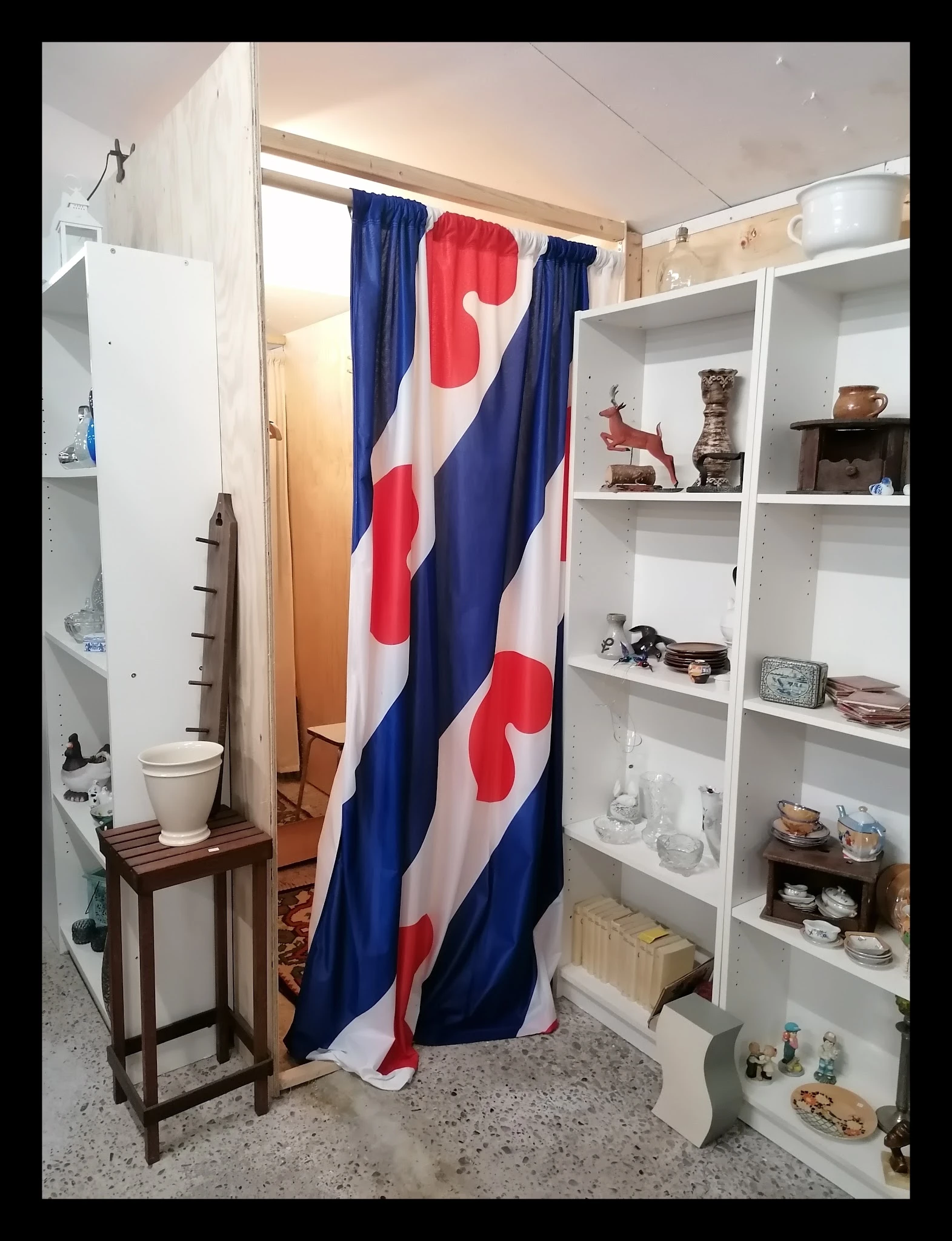 Winkelinterieur met witte stellingen, inboedelspullen en Nederlandse vlag als gordijn