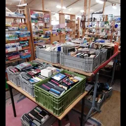 Plastic kratten met boeken op tafels in de winkel, stellingen met diverse artikelen op de achtergrond