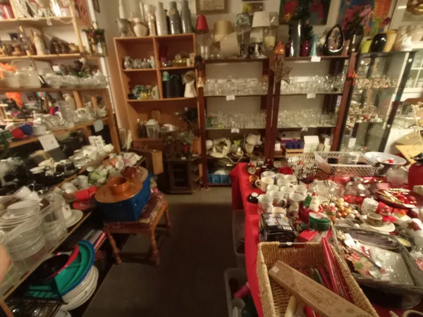 Winkelvloer met tafels vol verzamelde spullen, houten kasten en stellingen met serviesgoed en decoraties