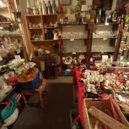 Winkelvloer met tafels vol verzamelde spullen, houten kasten en stellingen met serviesgoed en decoraties