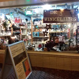 Winkelinterieur met uitgestalde spullen achter glas, winkelnavn 'De Winkeliers' zichtbaar op bord