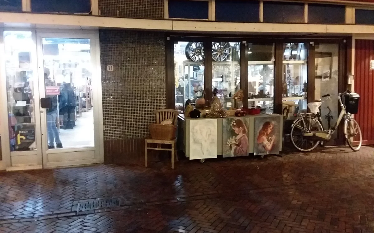 Winkelgevel met etalage, ingang en uitgestalde tweedehandsartikelen waaronder fiets en meubels