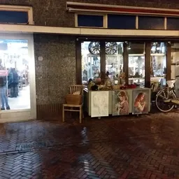 Winkelgevel met etalage, ingang en uitgestalde tweedehandsartikelen waaronder fiets en meubels