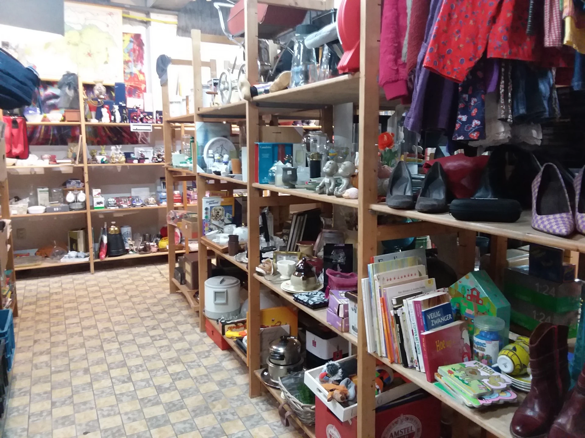 Houten stellingen met diverse tweedehands spullen, kleding, boeken en huishoudartikelen in kringloopwinkel
