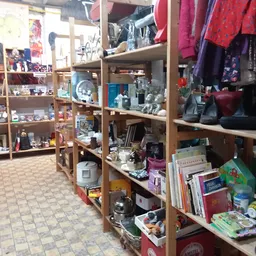 Houten stellingen met diverse tweedehands spullen, kleding, boeken en huishoudartikelen in kringloopwinkel
