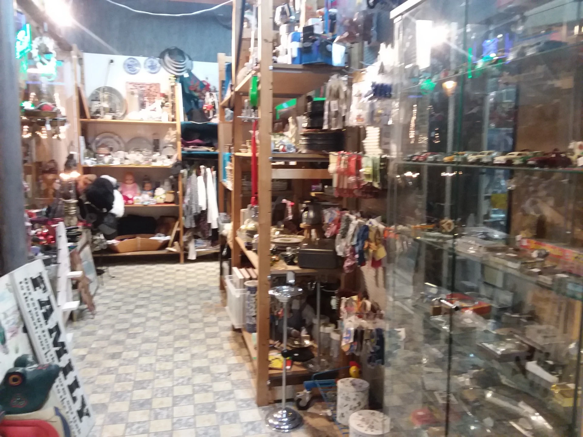 Binnenaanzicht van kringloopwinkel met display-kasten, stellingen en diverse uitgestalde spullen
