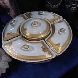 Decoratief porseleinen servies met goudkleurige versiering, bestaande uit een centrale schaal met vier uitstulpingen