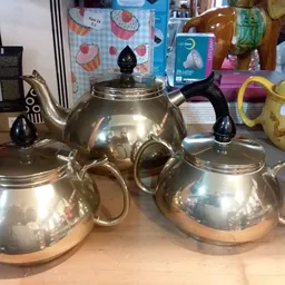 Drie zilveren theepotten met zwarte handvatten en deksels, uitgestald op een tafel
