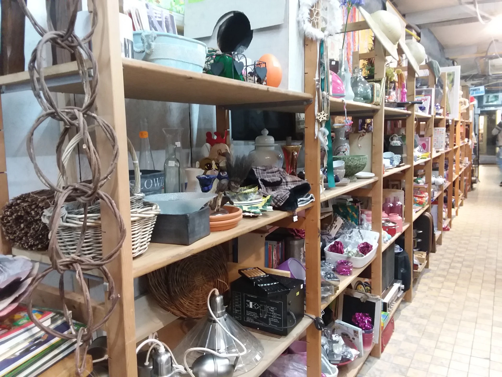 Houten stellingen met diverse huishoudelijke artikelen, decoratie en tweedehands spullen in een kringloopwinkel
