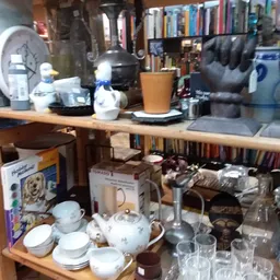 Stellingen met serviesgoed, glazen, boeken en huishoudartikelen in een kringloopwinkel