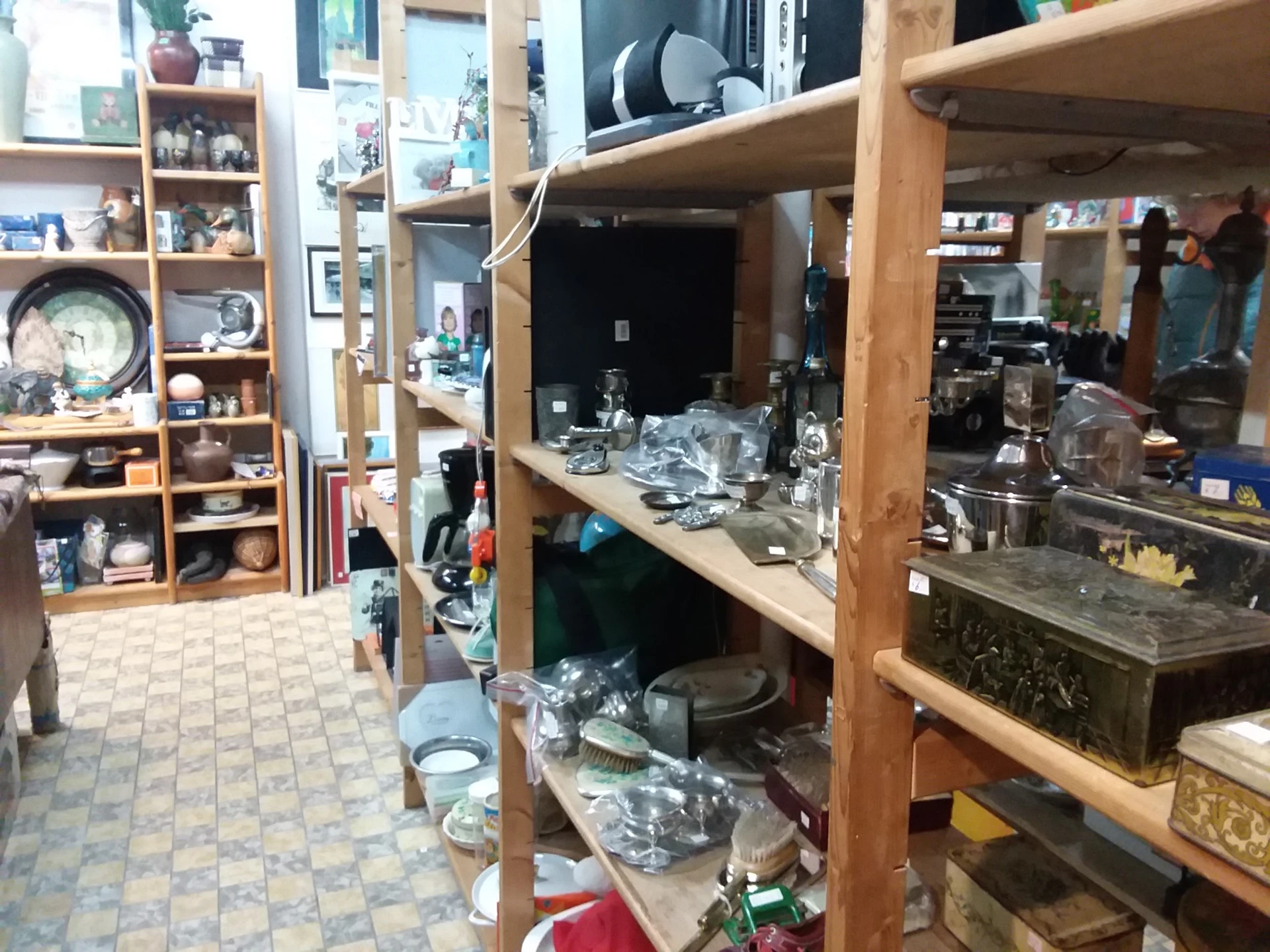 Houten stellingen met huishoudelijke spullen en serviesgoed in een rommelige kringloopwinkel