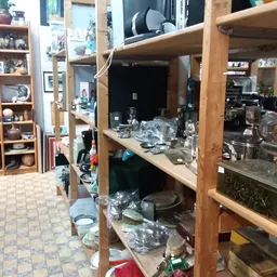 Houten stellingen met huishoudelijke spullen en serviesgoed in een rommelige kringloopwinkel