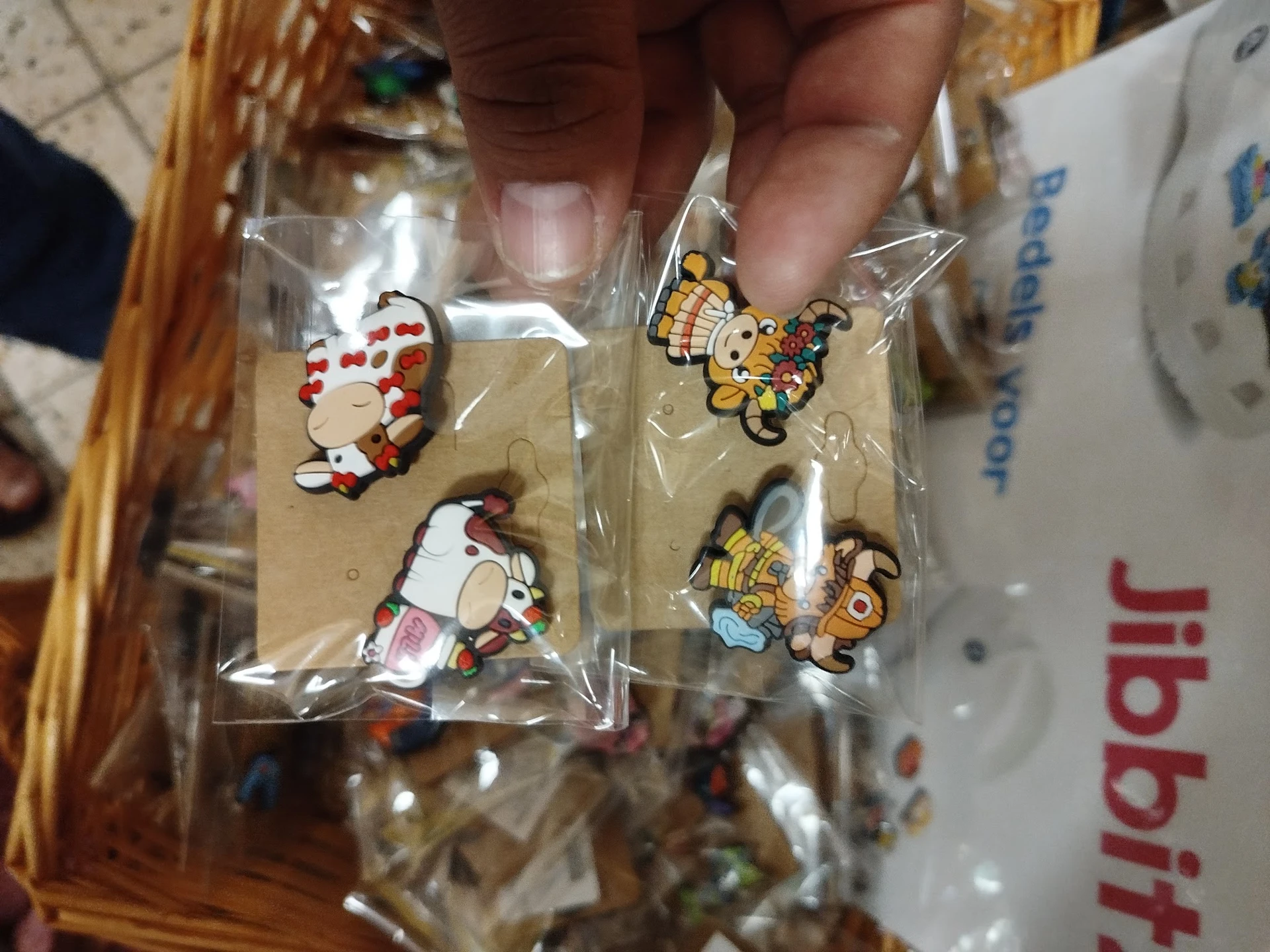 Close-up van vier kleine decoratieve pins of broche's in plastic verpakking met figuren in rood-wit en geel-bruin design