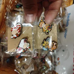 Close-up van vier kleine decoratieve pins of broche's in plastic verpakking met figuren in rood-wit en geel-bruin design