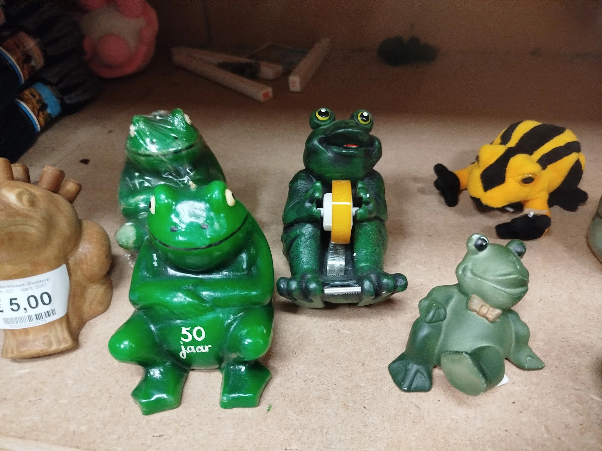 Verzameling speelgoedfiguren op display: groene kikker, donkergroene kikker met geel, gele bij en lichtgroene kikker