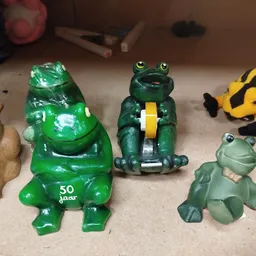 Verzameling speelgoedfiguren op display: groene kikker, donkergroene kikker met geel, gele bij en lichtgroene kikker