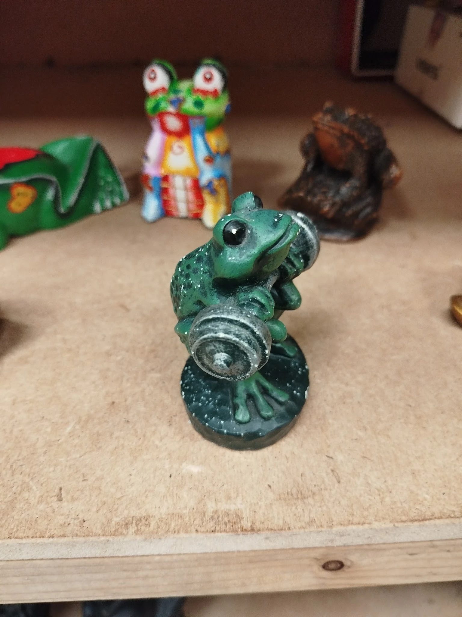 Groen beschilderd beeld van een kikker met zilveren accenten, close-up op neutrale achtergrond