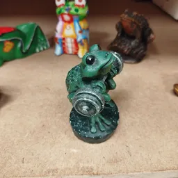 Groen beschilderd beeld van een kikker met zilveren accenten, close-up op neutrale achtergrond