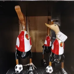 Twee rode en witte vogelhuisjes met houten dakjes en gele embleem, aan houten stokjes opgehangen in een vitrine.