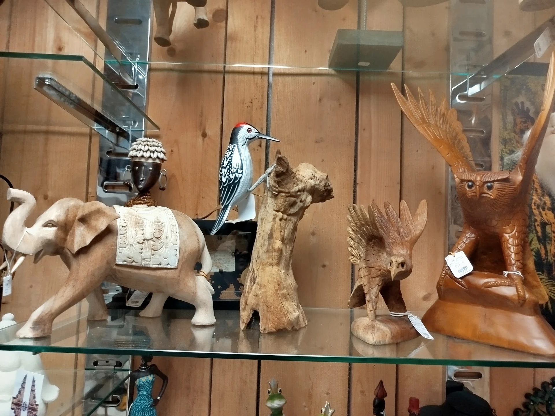 Glazen vitrine met diverse houten beeldjes en decoratieve objecten zoals olifant, vogels en andere kunstvoorwerpen