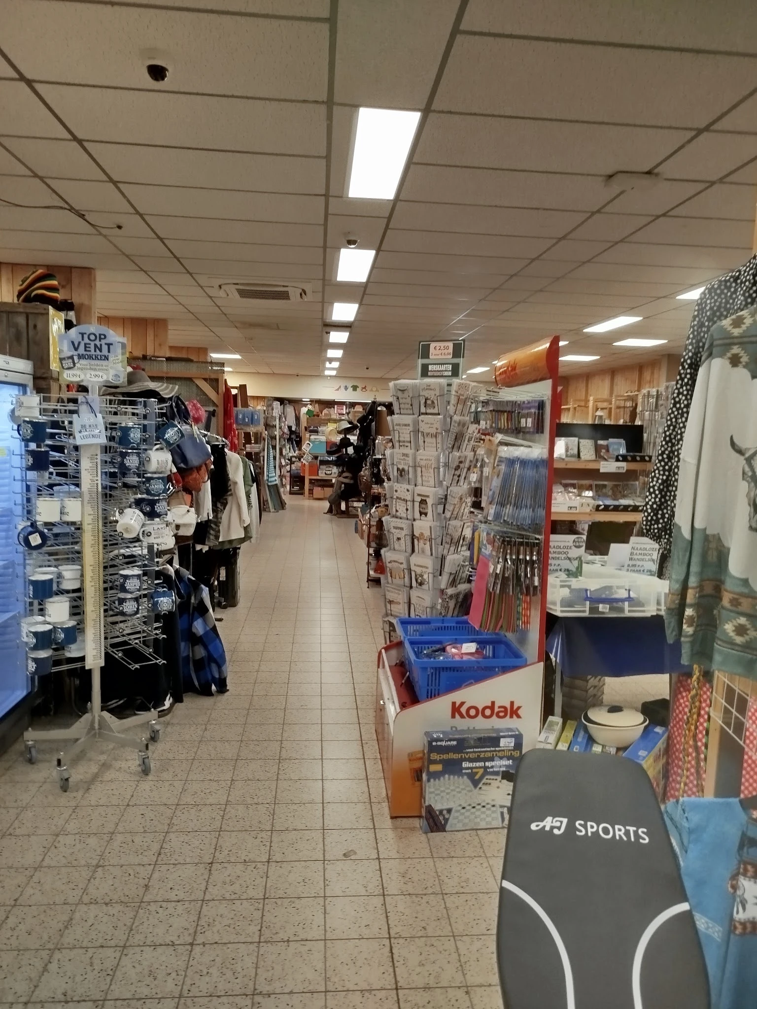 Binnenaanzicht van kringloopwinkel met stellingen, kleding aan hangers, boeken en huishoudartikelen langs de wanden