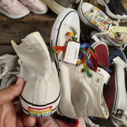 Witte sneaker met kleurrijke papegaai-decoratie en gekleurde veter, close-up van schoen in hand