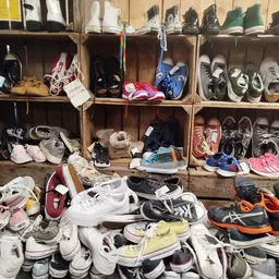 Uitgestalde tweedehands schoenen en sneakers op stellingen en op de grond in de kringloopwinkel