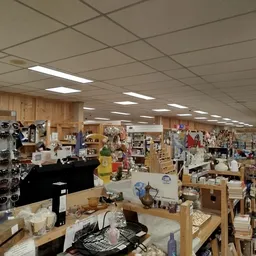 Ruim winkelbinnenland met stellingen vol tweedehands spullen, kleding en huishoudartikelen onder fluorescent licht