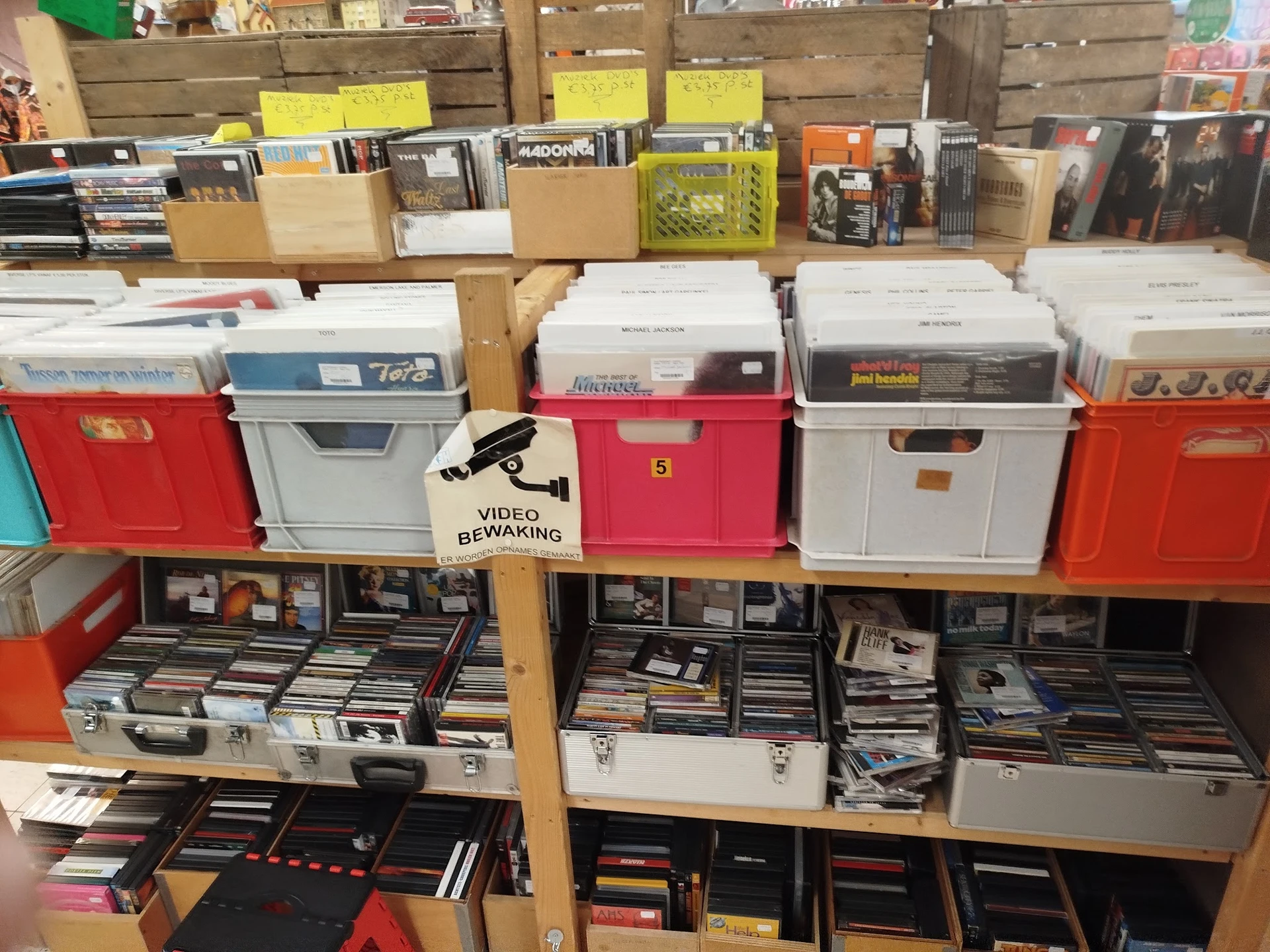 Planken met dvd's, cd's en ander media in dozen en bakken georganiseerd in de winkel