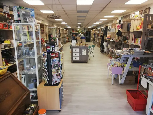 Winkelvloer van kringloopwinkel met stellingen vol artikelen, tafels met spullen en overhead verlichting