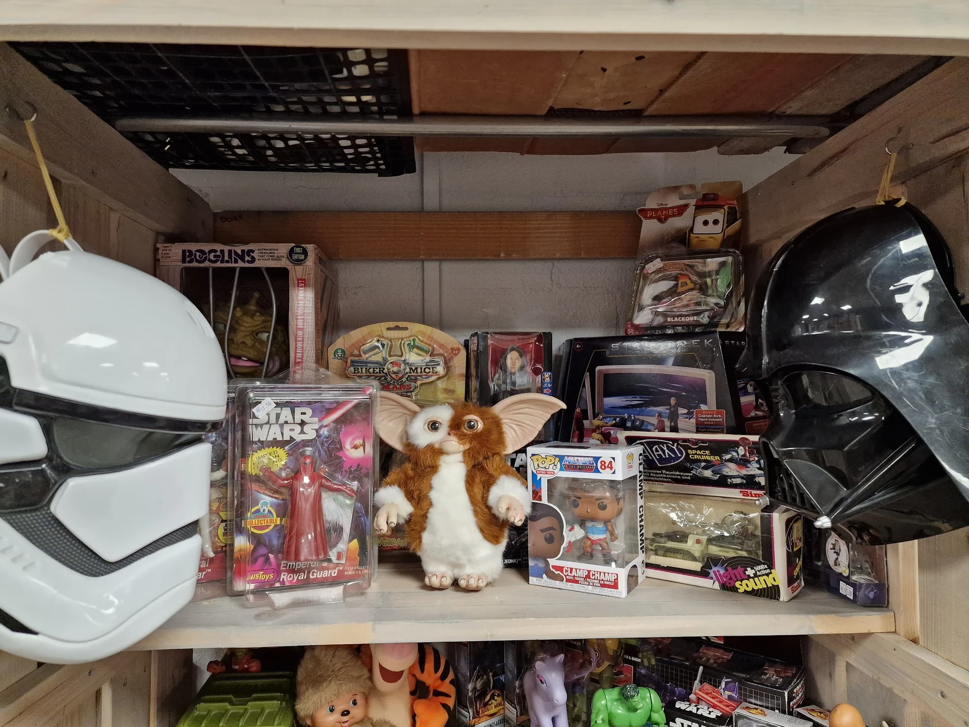 Kastplank met speelgoed en verzamelobjecten: actiefiguren, Gremlins-pop, Star Wars-verpakking en vintage speelgoedauto's