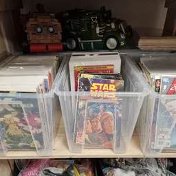 Plastic bakken met verzameling strips, stripboeken en comicboeken netjes uitgestald op een plank