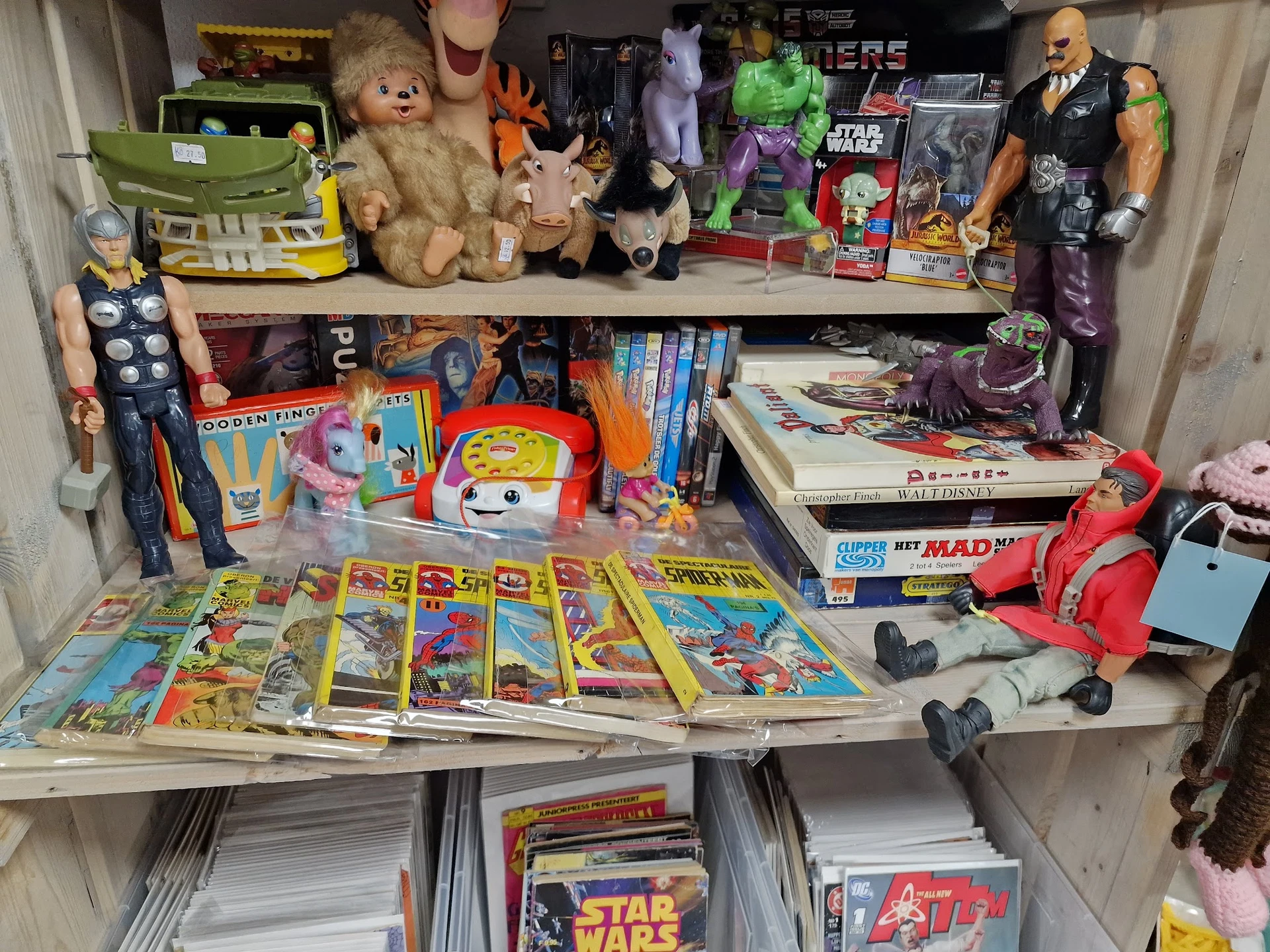 Uitgestalde collectie speelgoed, poppen, stripboeken en actiefiguren op planken en tafels
