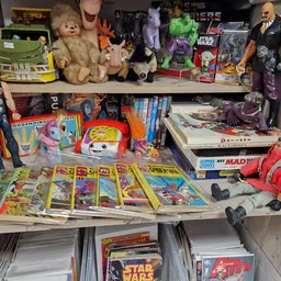 Uitgestalde collectie speelgoed, poppen, stripboeken en actiefiguren op planken en tafels