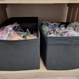 Twee grijze bakken vol met verschillende tweedehands textiel en kleding in een winkelkast