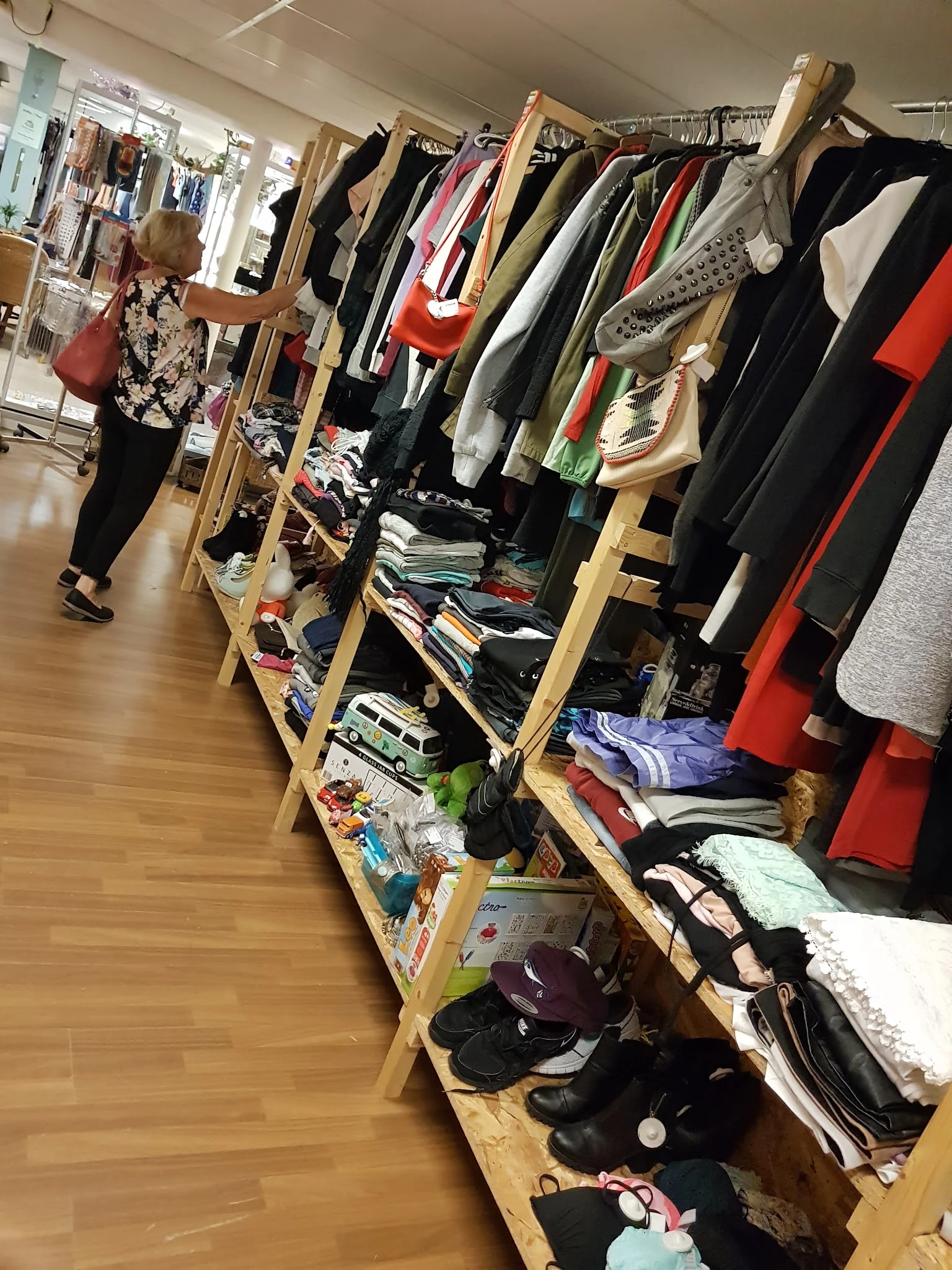 Houten stellingen met diverse tweedehands kleding, schoenen en accessoires in een kringloopwinkel