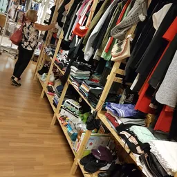 Houten stellingen met diverse tweedehands kleding, schoenen en accessoires in een kringloopwinkel
