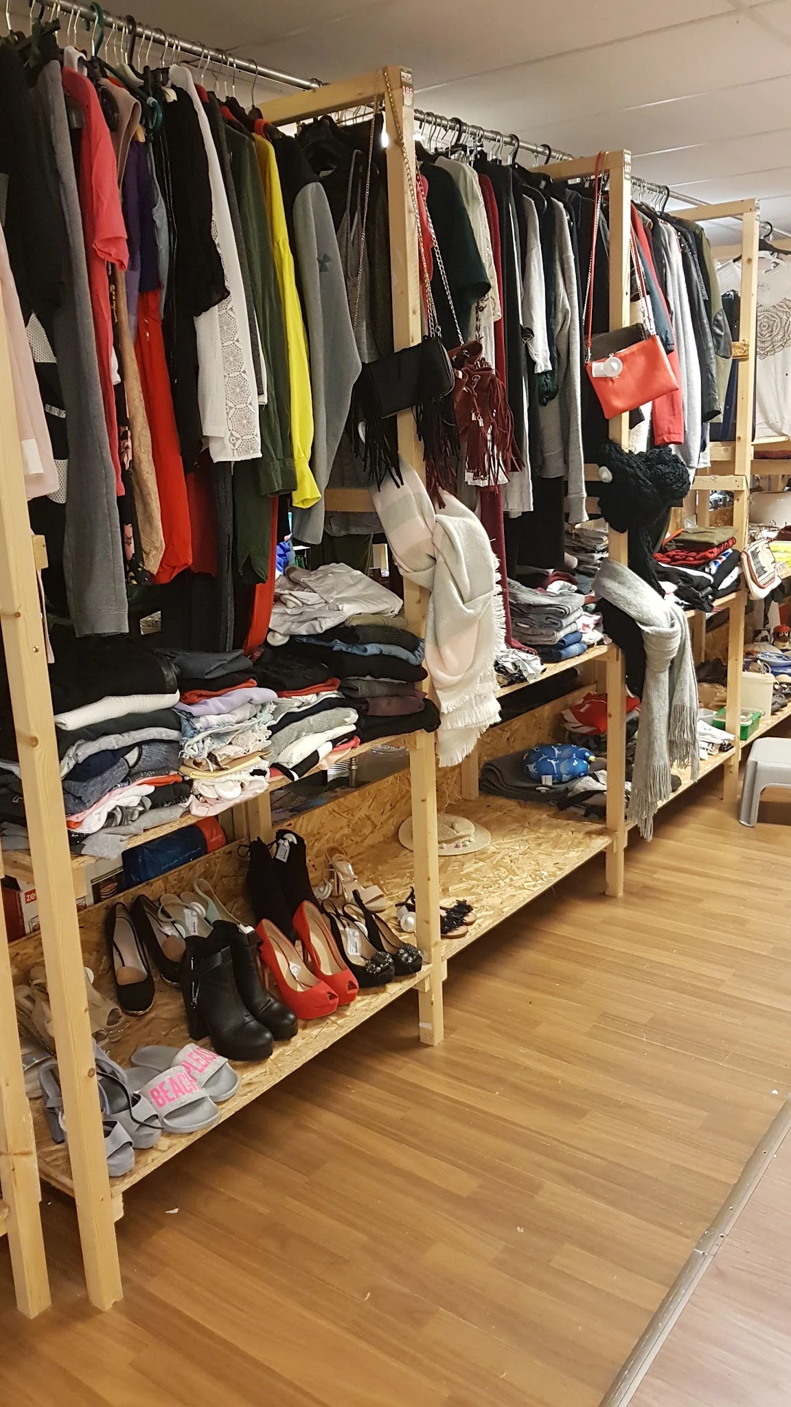 Houten stellingen met uitgestalde tweedehands kleding, schoenen en accessoires in de winkel