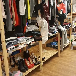 Houten stellingen met uitgestalde tweedehands kleding, schoenen en accessoires in de winkel