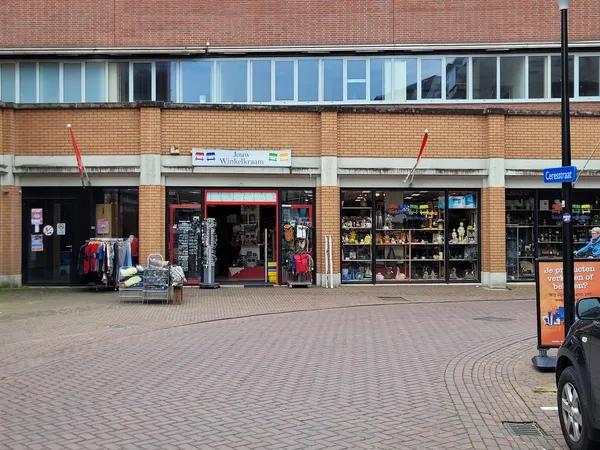 Gevel van kringloopwinkel met etalages vol spullen, rode pui en grote ramen op bakstenen gebouw