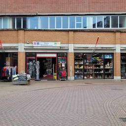 Gevel van kringloopwinkel met etalages vol spullen, rode pui en grote ramen op bakstenen gebouw