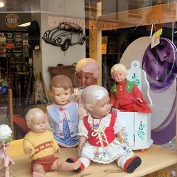 Uitgestalde vintage poppen en speelgoed in een kringloopwinkel, met auto-decoratie en paarse hoed op achtergrond