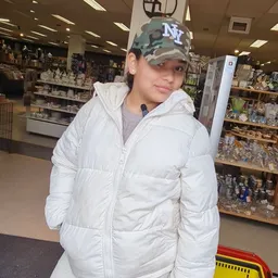 Jongeman in witte jas en camouflage cap in een winkelinterieur