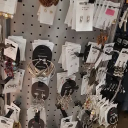 Uitgestalde sieradenrekken met oorbellen, armbanden en kettingen op een grijze pegboard-wand